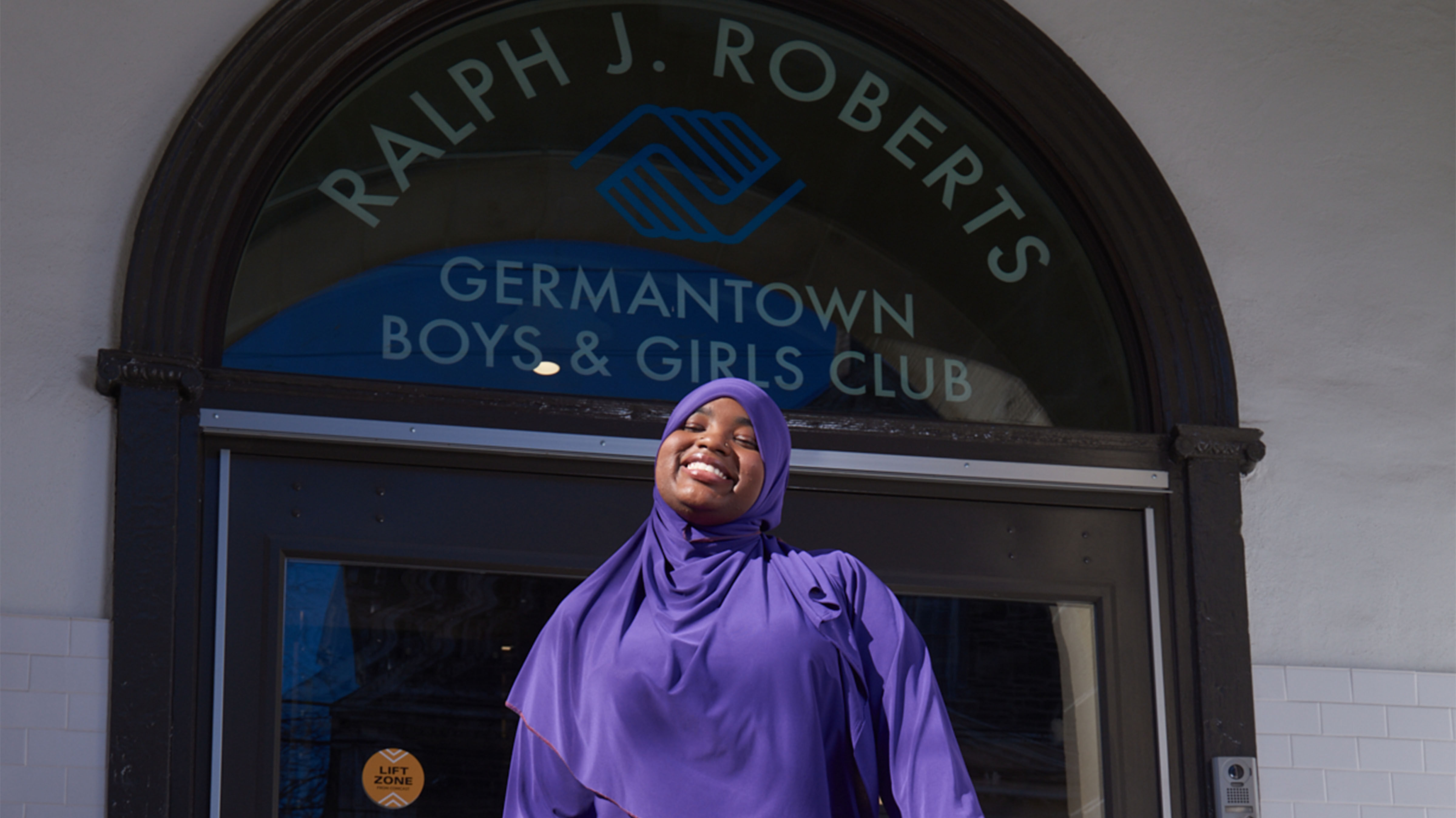 A student standing in front of the Ralph J. Roberts Germantown Boys & Girls Club.