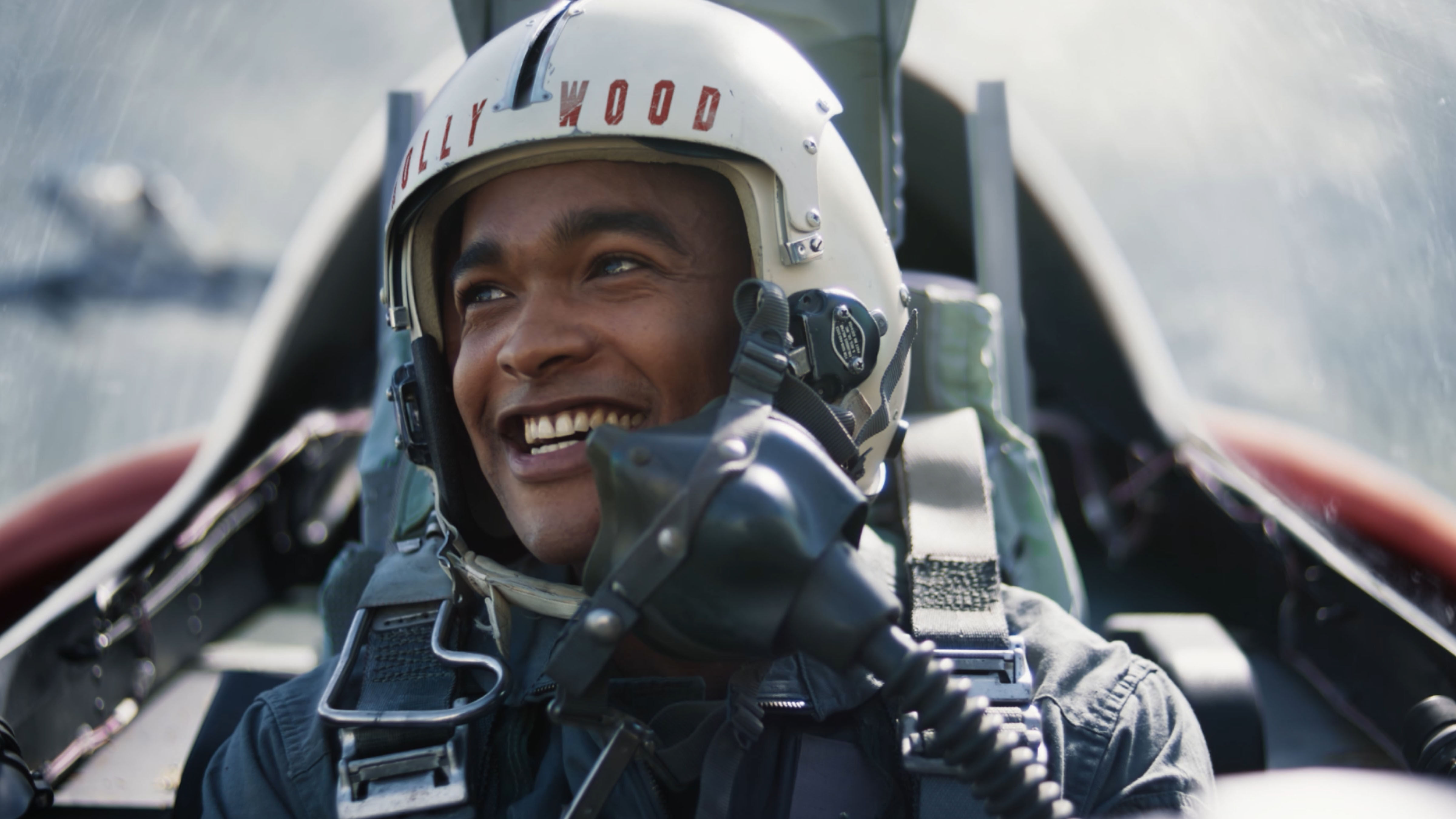 A young man flying an army plane, smiling off into the distance.